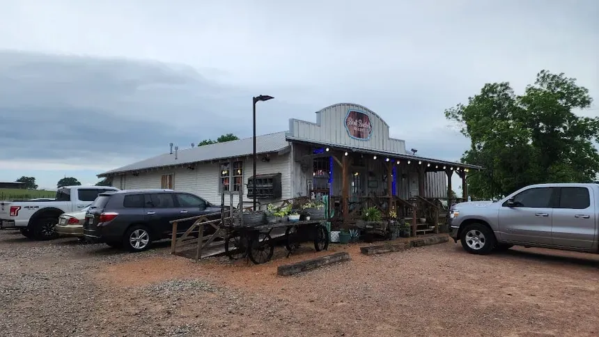 The Bent Bucket Bakery storefront: a long weathered timber building with a covered porch and a curved sign board on the roof